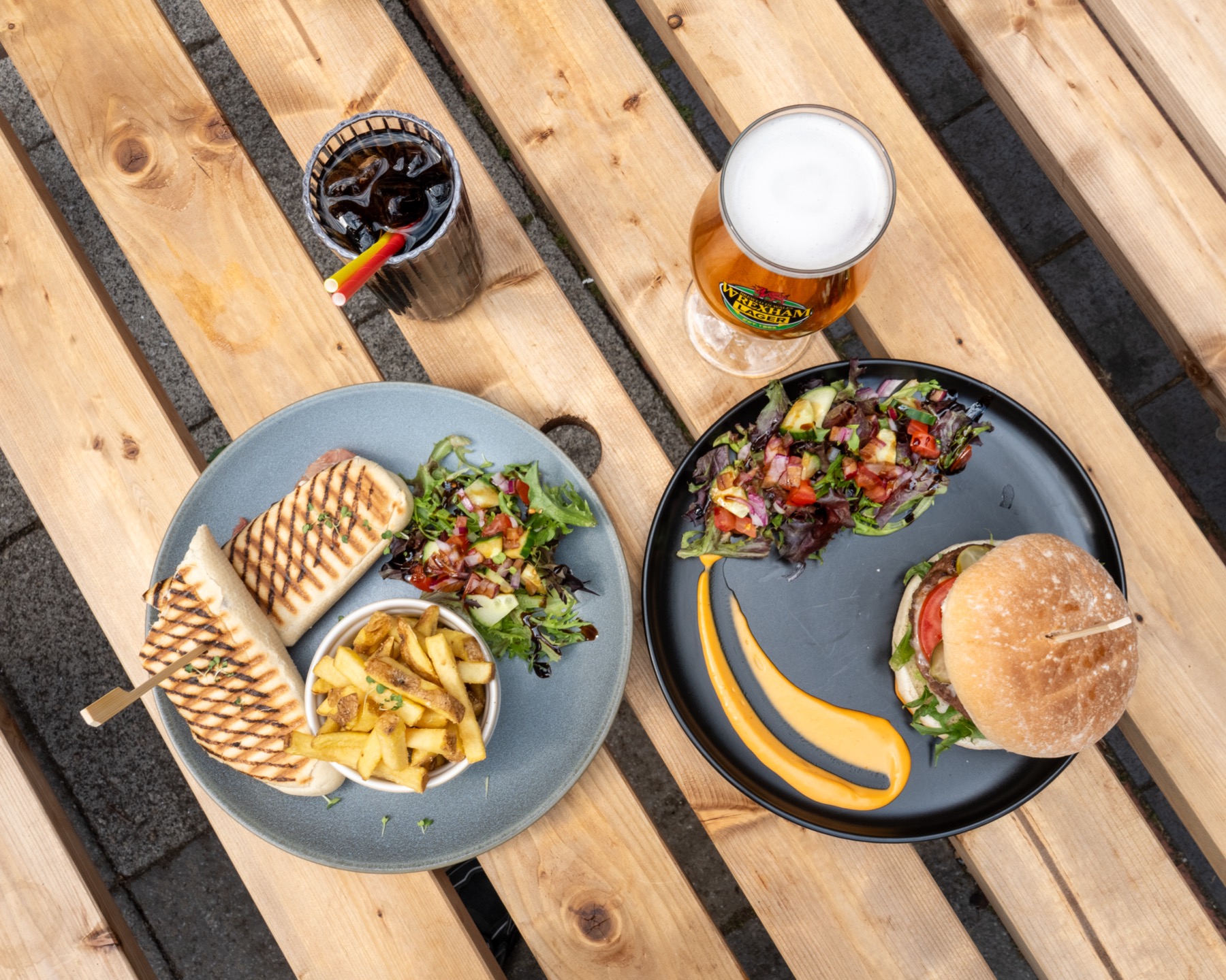 A burger, panini, chips, salad and drinks served on a wooden table at Heaven Coffee Shop